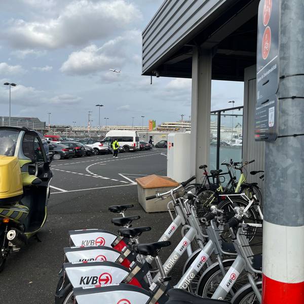 Leihräder mit der Aufschrift „KVB“ auf einem Parkplatz, im Hintergrund sieht man den Flughafen Köln/Bonn