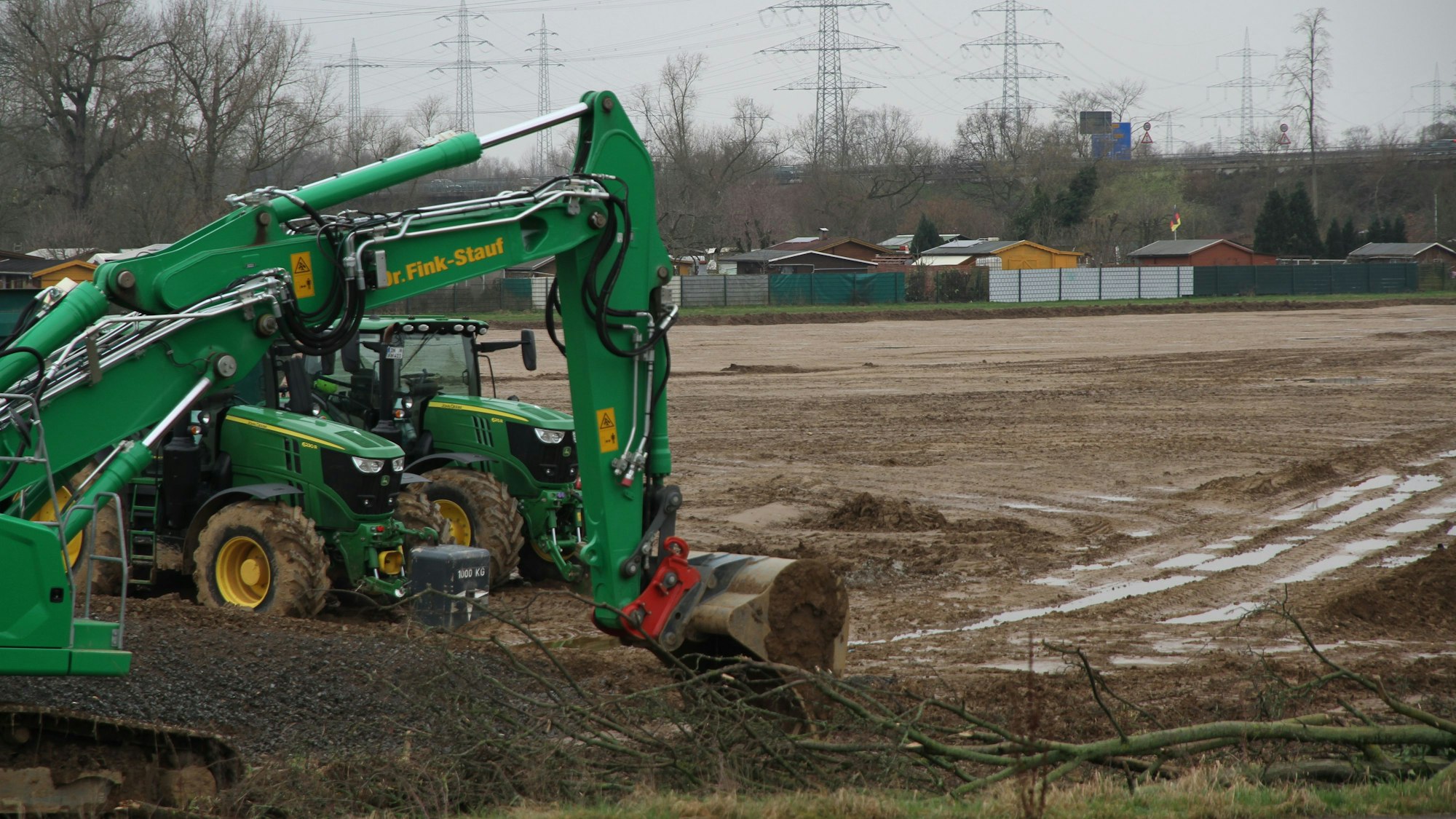 Ein grüner Bagger und zwei grüne Traktoren an einer Baugrube