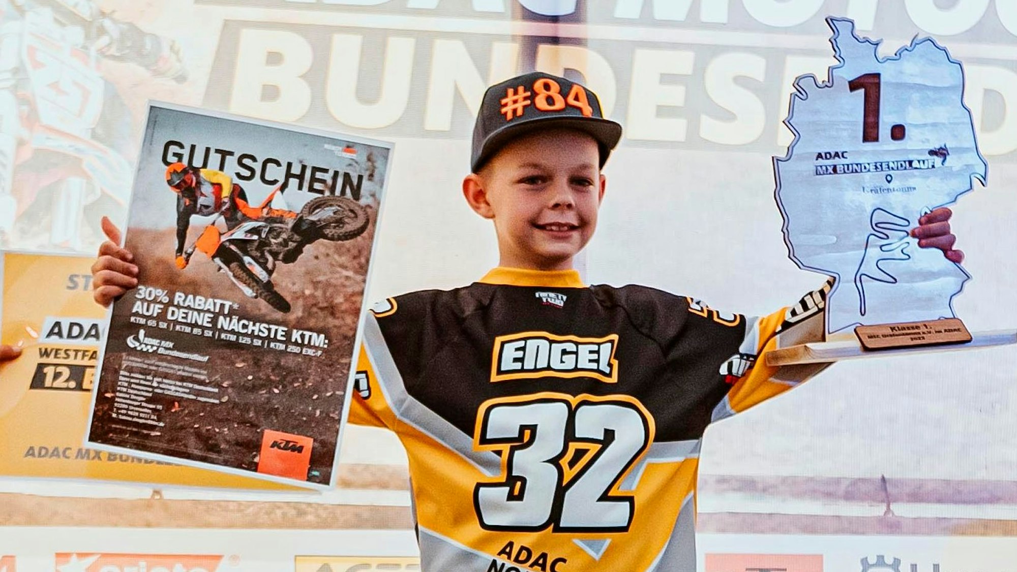 John Engel aus Kuchenheim hält in der einen Hand einen Gutschein, in der anderen den Pokal in Form der Umrisse Deutschlands, darauf steht die Platzierung 1.