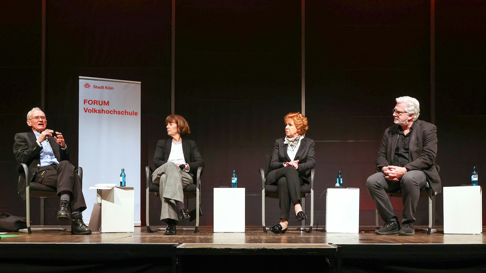 Zu sehen ist auf einer Bühne Oberbürgermeisterin Henriette Reker, wie sie mit Pfarrer Franz Meurer, Barbara Havlitza, Ministerin der Justiz a.D. und Beauftragte für den Opferschutz des Landes Nordrhein-Westfalen und Helmut Frangenberg über das Messer-Attentat auf sie und die Drohungen gegen sie bis heute spricht.