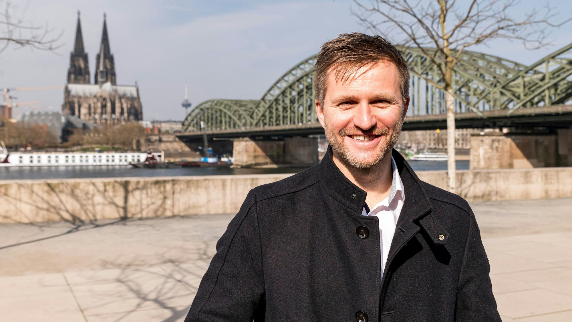 Nico Rathman steht vor dem Rheinboulevard in Köln-Deutz, im Hintergrund die Domspitzen