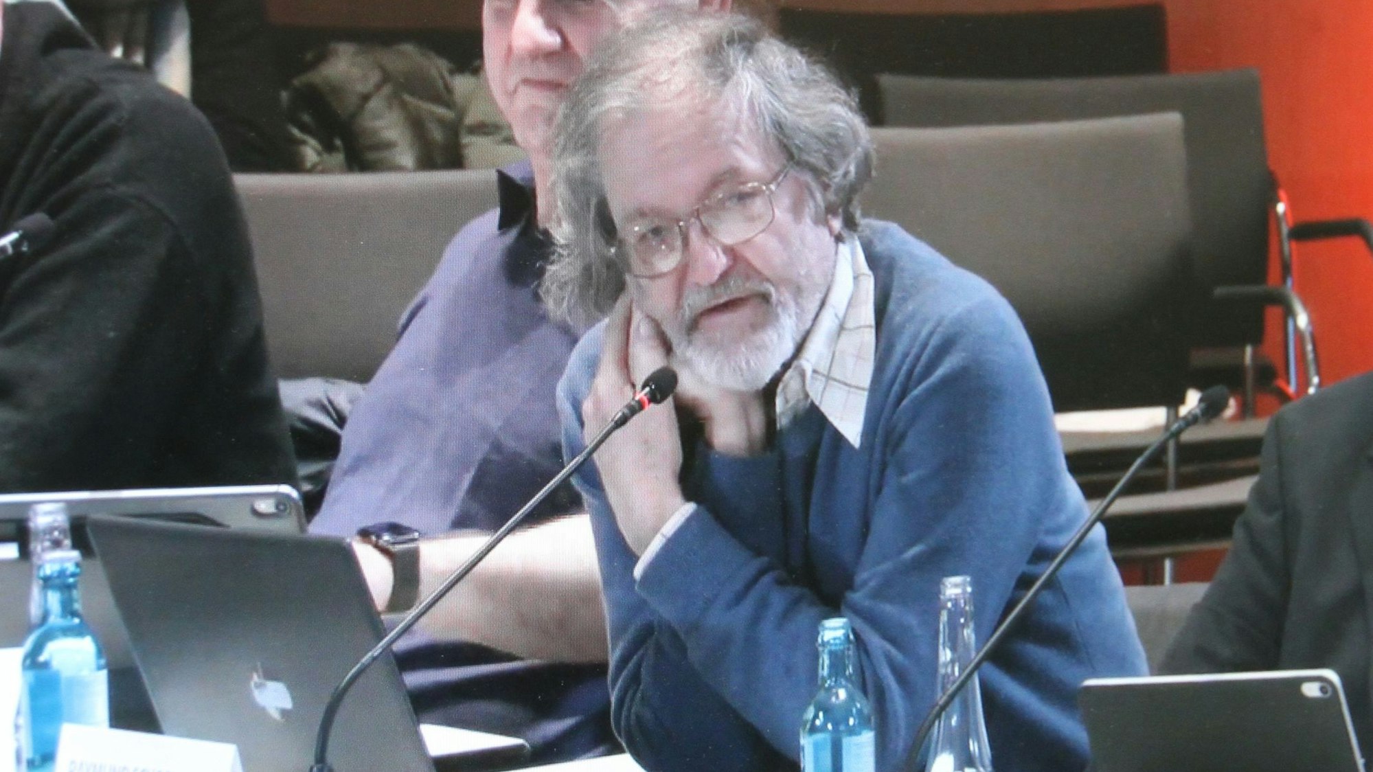 Ein Mann an einem Mikrophon an seinem Tisch in einem Ratsaal