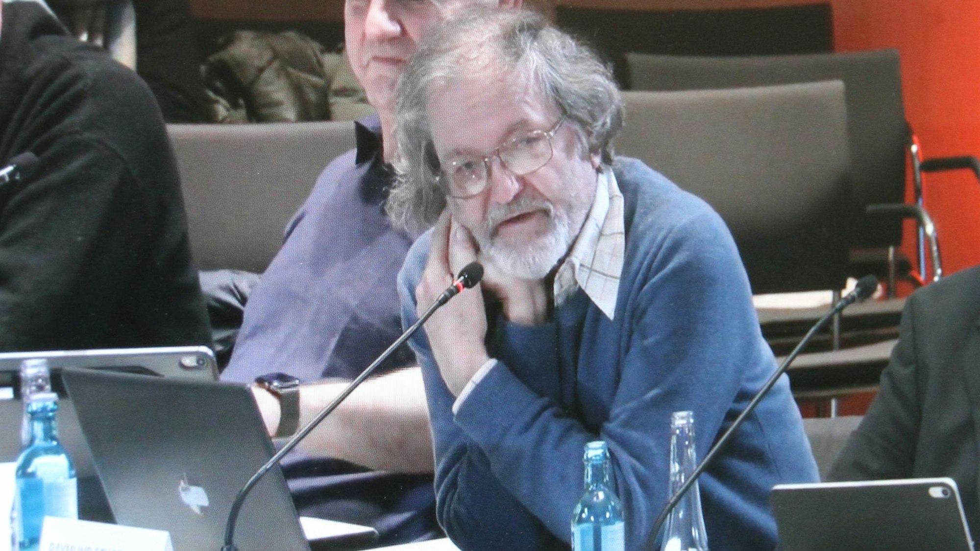 Ein Mann an einem Mikrophon an seinem Tisch in einem Ratsaal