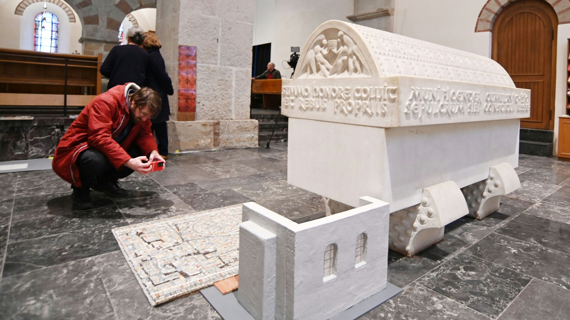 Zu sehen sind ein weißer Sarkophag und ein Bodenmosaik.