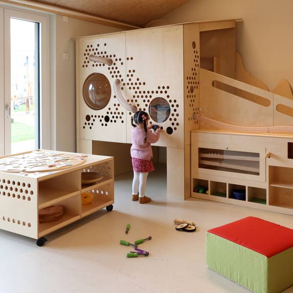 Blick in einen Gruppenraum einer Kita. Ein Kind spielt an einer Holzwand.