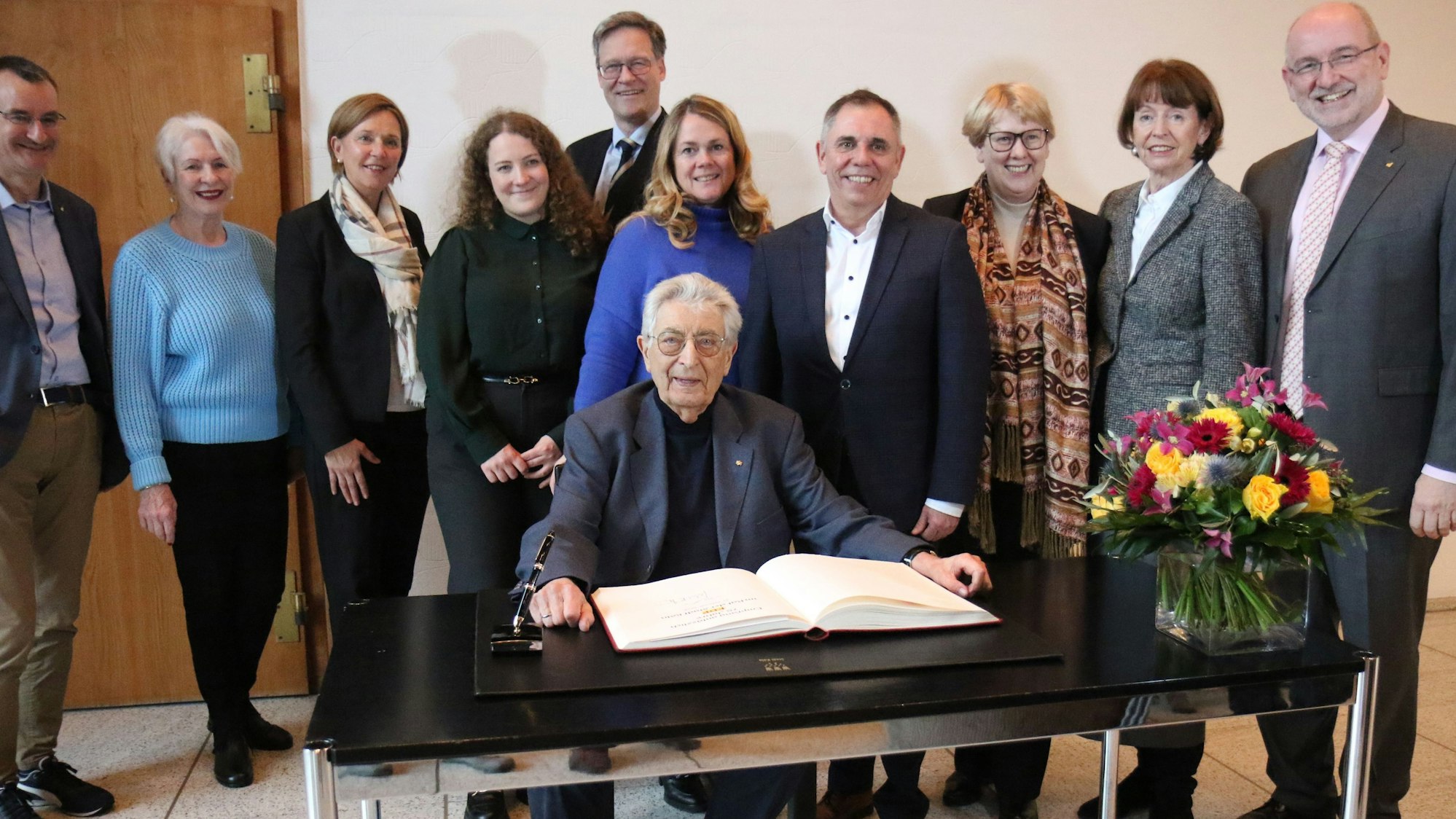 Zu sehen sind zehn Menschen nebeneinander stehend in der Vorderansicht. Gerhard Baum sitzt davor.