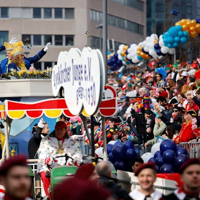 Jecke stehen auf einer Tribüne und verfolgen den Rosenmontagszug.