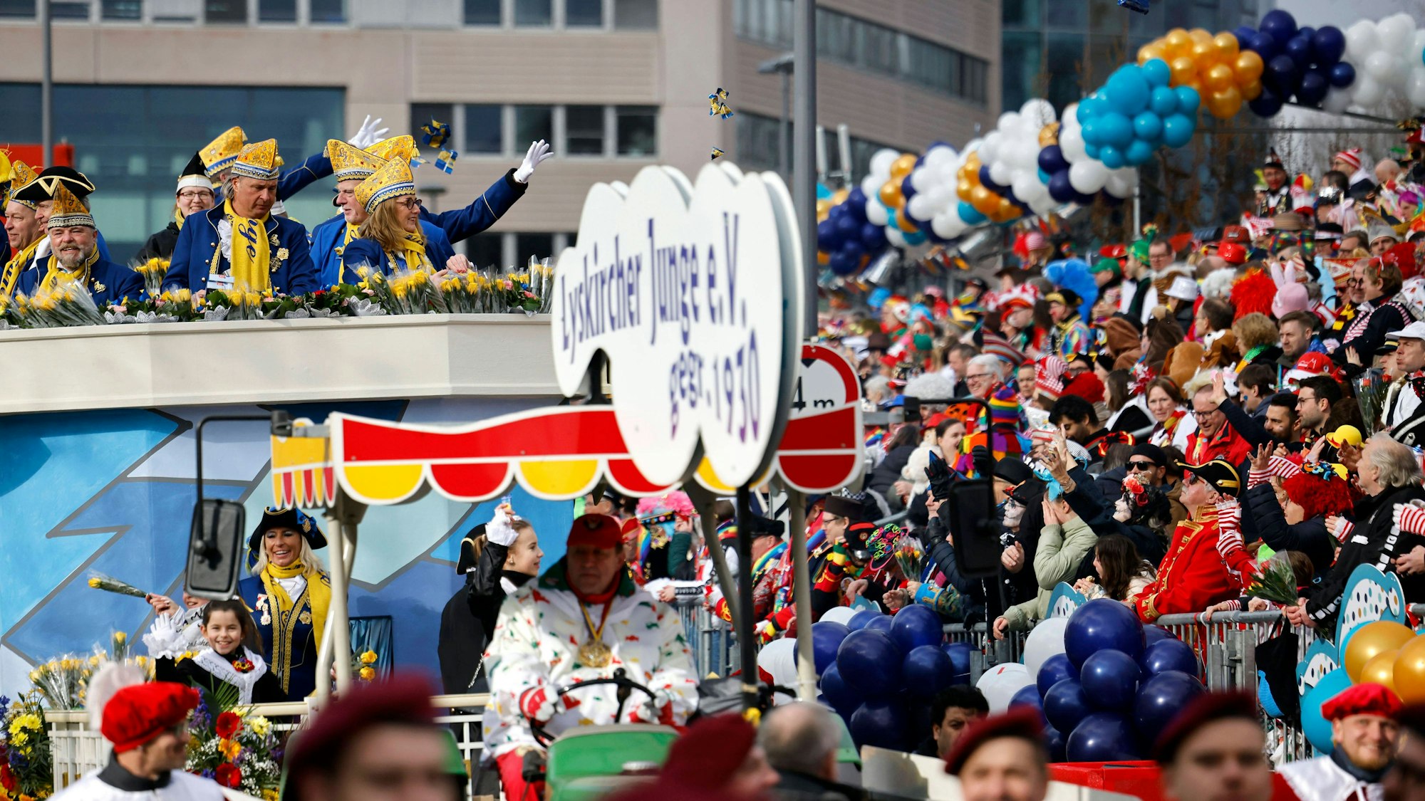 Jecken auf einer Tribüne und kostümierte Narren auf dem Rosenmontagszug 2023 unter dem Motto 200 Jahre Kölner Karneval Ov Krüz oder quer in Köln. In diesem Jahr startet der Zug erstmalig auf der rechten Rheinseite. Dadurch will man beide Rheinseiten stärker miteinander verbinden.