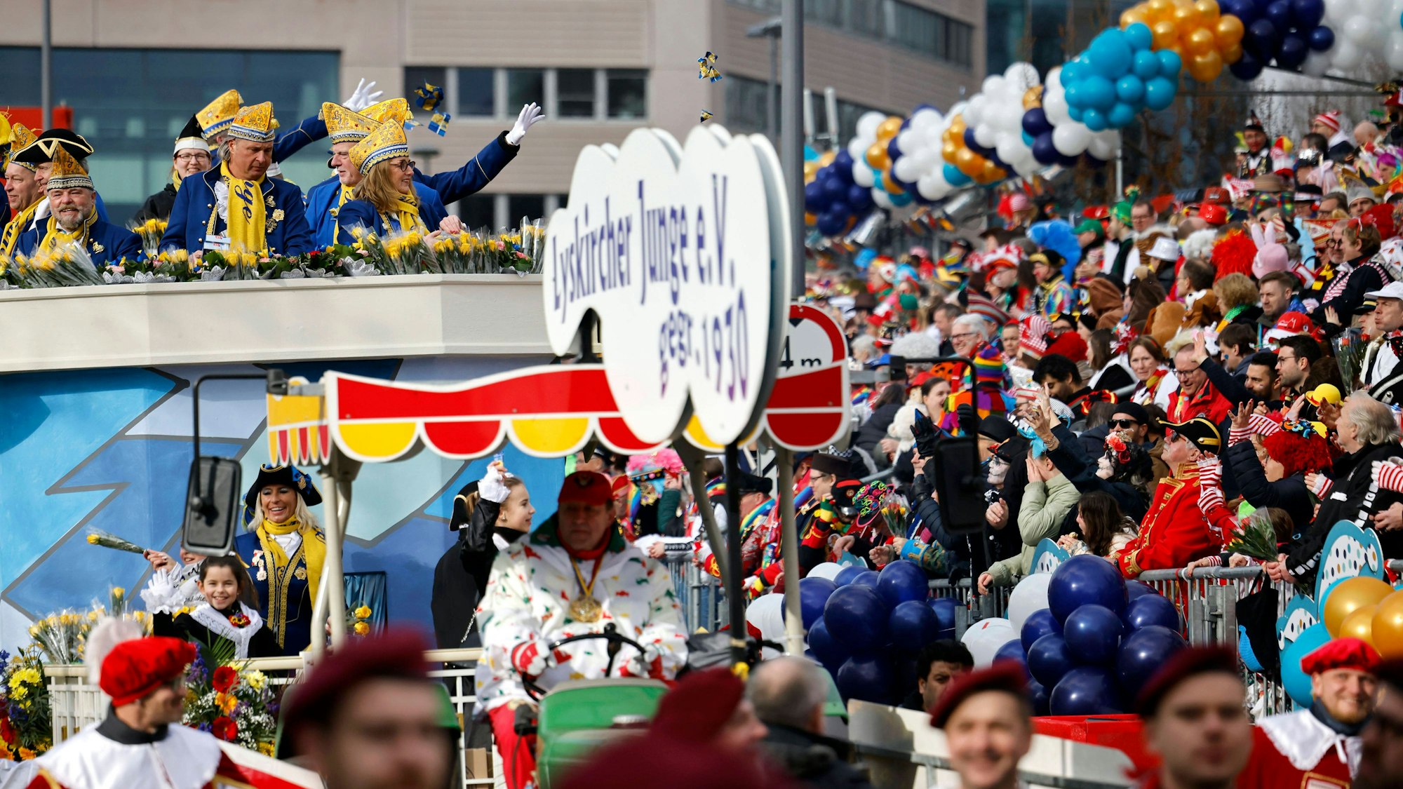 Jecke stehen auf einer Tribüne und verfolgen den Rosenmontagszug.