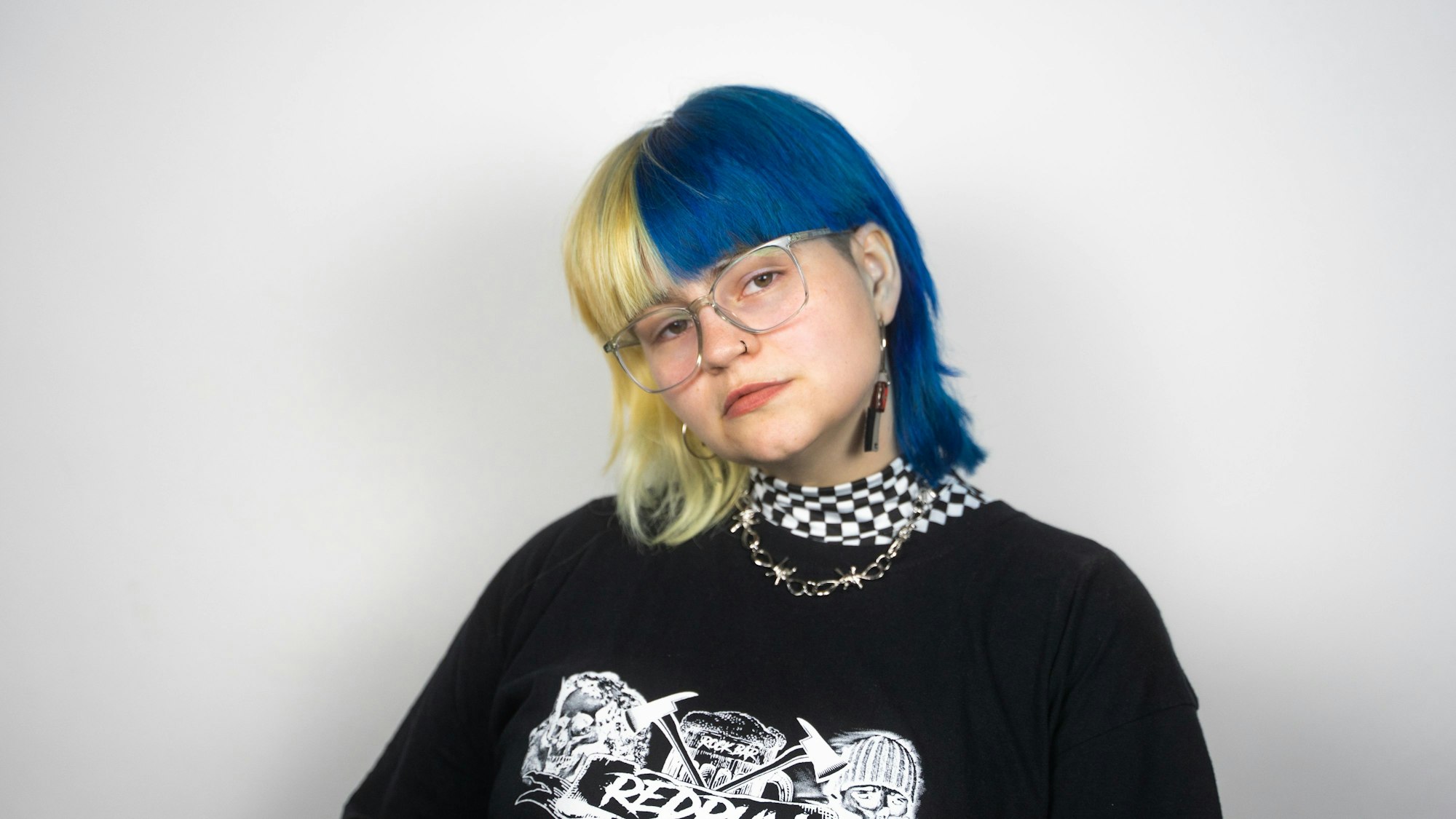Eine junge Frau mit blond-blauen Haaren, Brille und einem schwarzen T-Shirt mit Aufdruck.