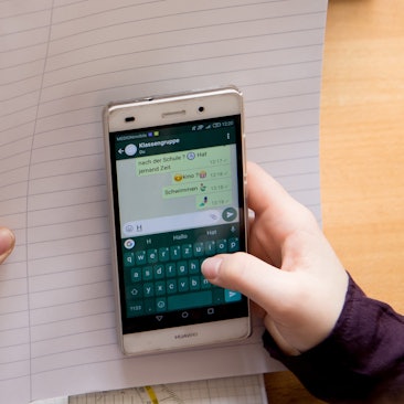 Eine Schülerin sitzt mit ihrem Handy und ihren Schulsachen an einem Schreibtisch.