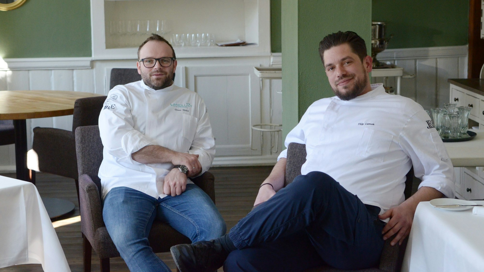 Der Restaurantführer Guide Michelin zeichnet Bembergs Häuschen in Euskirchen-Flamersheim regelmäßig mit einem Michelin-Stern aus. Im Bild Geschäftsführer Oliver Röder (l.) und Küchenchef Filip Czmok (r.). Sie sitzen im Restaurant auf Sesseln und lächeln in die Kamera.