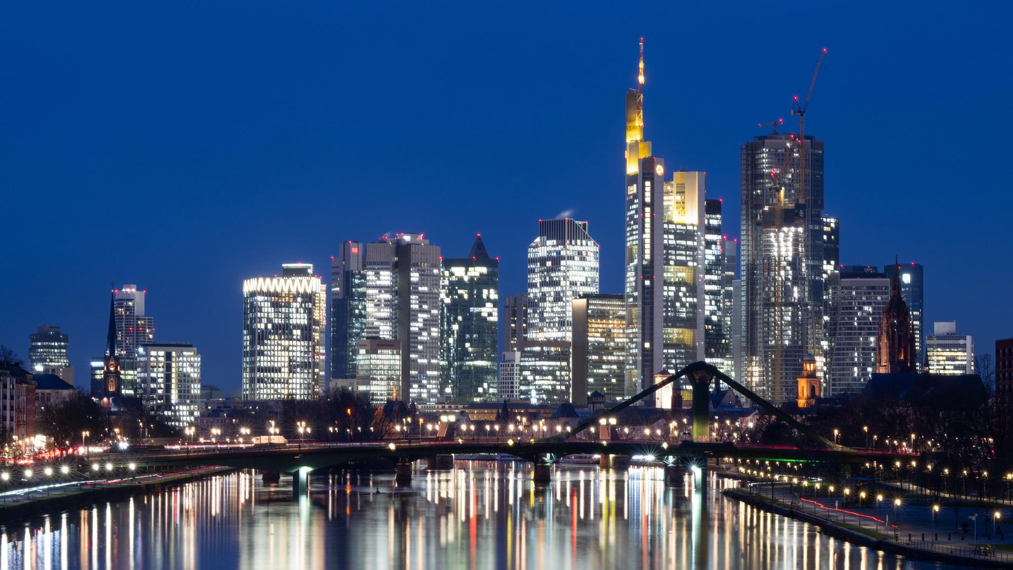 Die Lichter der Bankenskyline von Frankfurt am Main leuchten im letzten Licht des Tages.