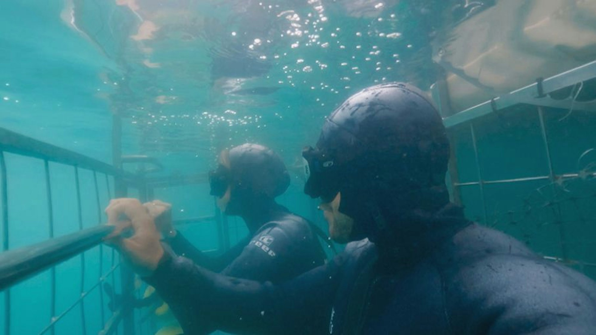 Eine Frau und ein Mann sind in Taucheranzügen in einem Käfig.