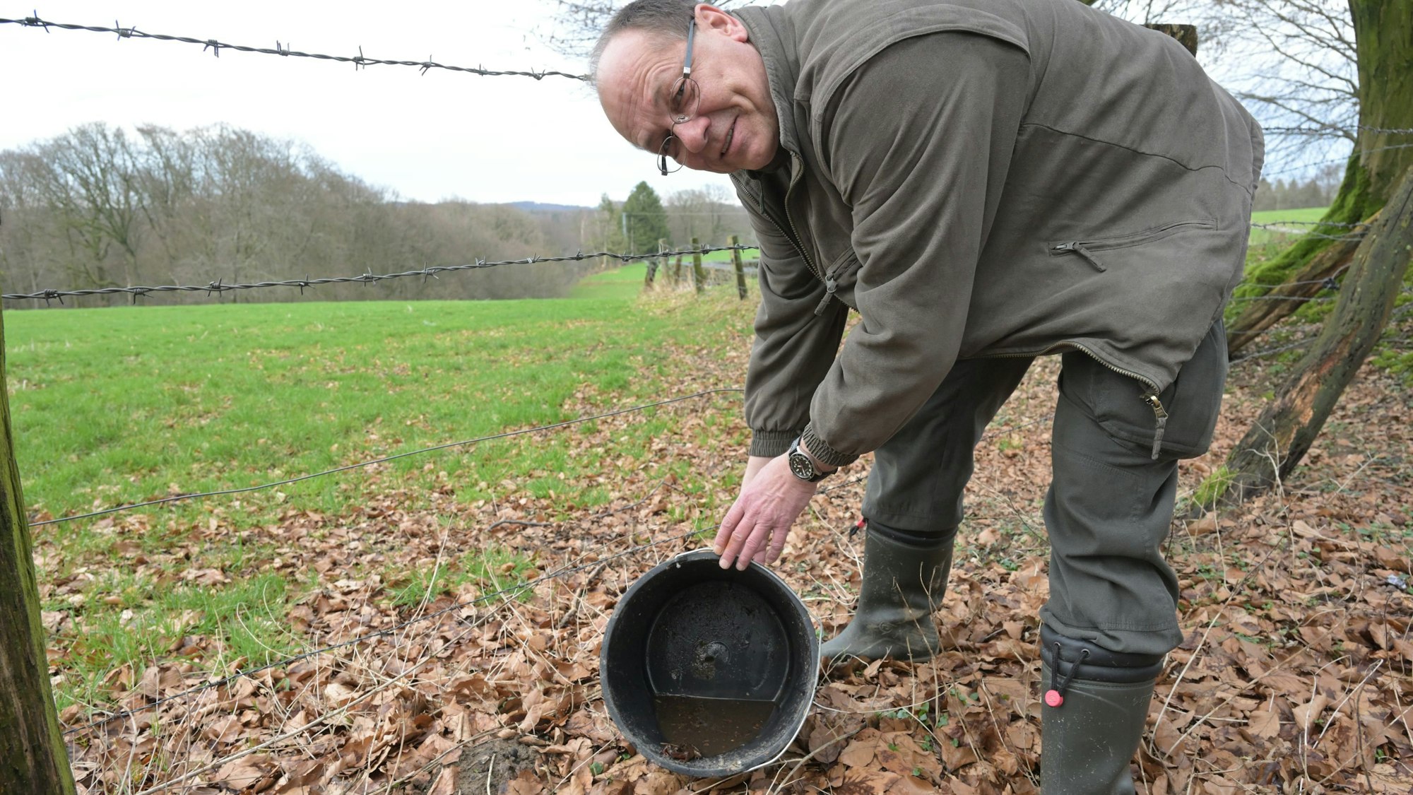 Ein Artenschützer leert vorsichtig auf einer Wiese einen Eimer aus, in dem ein Grasfrosch sitzt.
