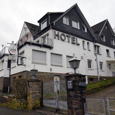 Ein großes Haus mit verschlossenen Fenstern und heruntergelassenen Rollläden steht an einer Straße, auf der Fassade ist der Schriftzug „Hotel“ zu lesen.