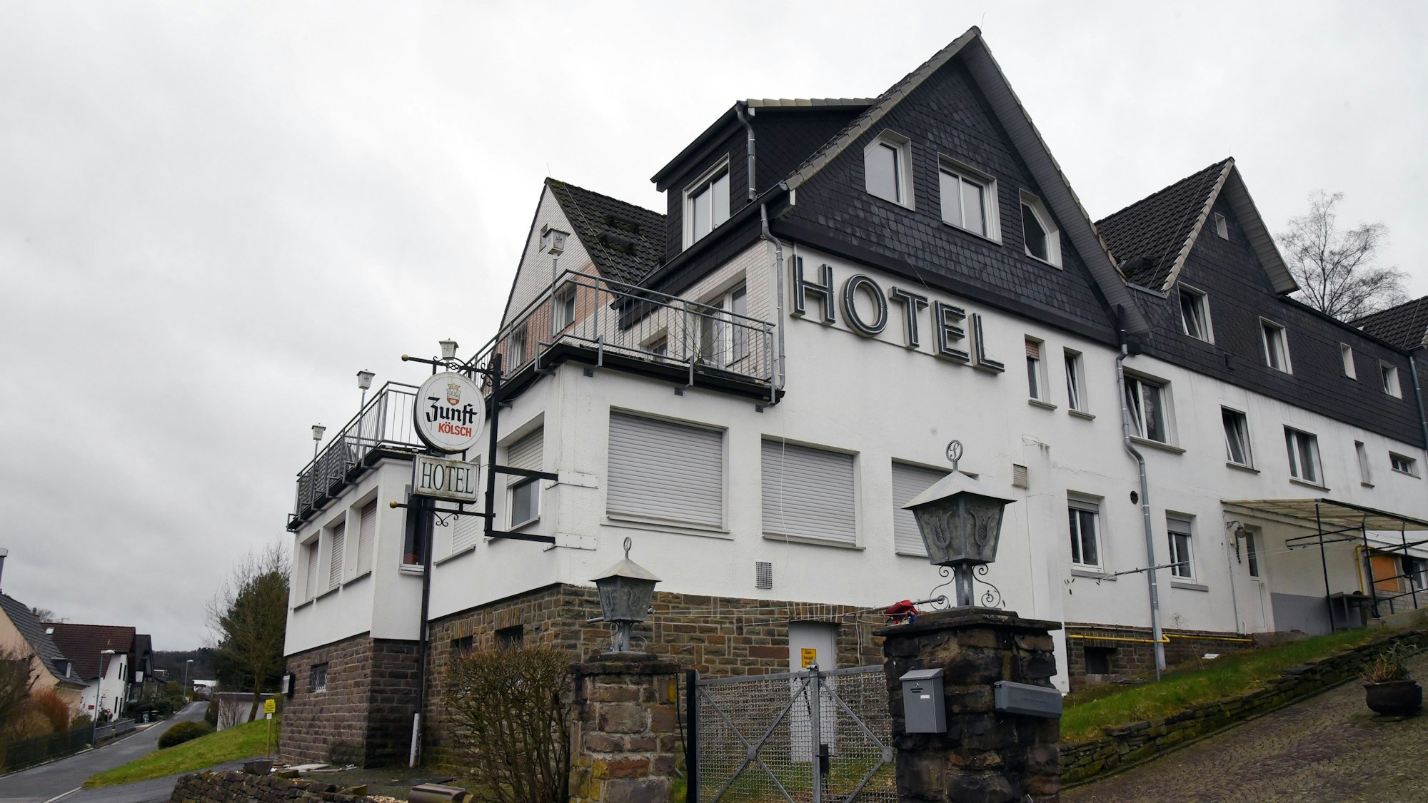 Ein großes Haus mit verschlossenen Fenstern und heruntergelassenen Rollläden steht an einer Straße, auf der Fassade ist der Schriftzug „Hotel“ zu lesen.