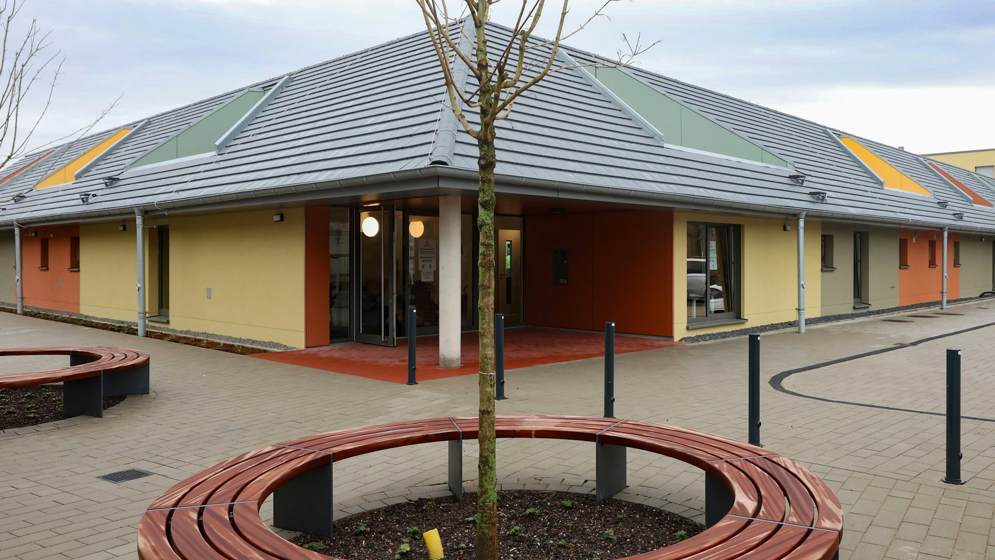 Zu sehen ist die neue Kindertagesstätte von außen. Im Vordergrund ist ein kleiner Baum zu sehen.