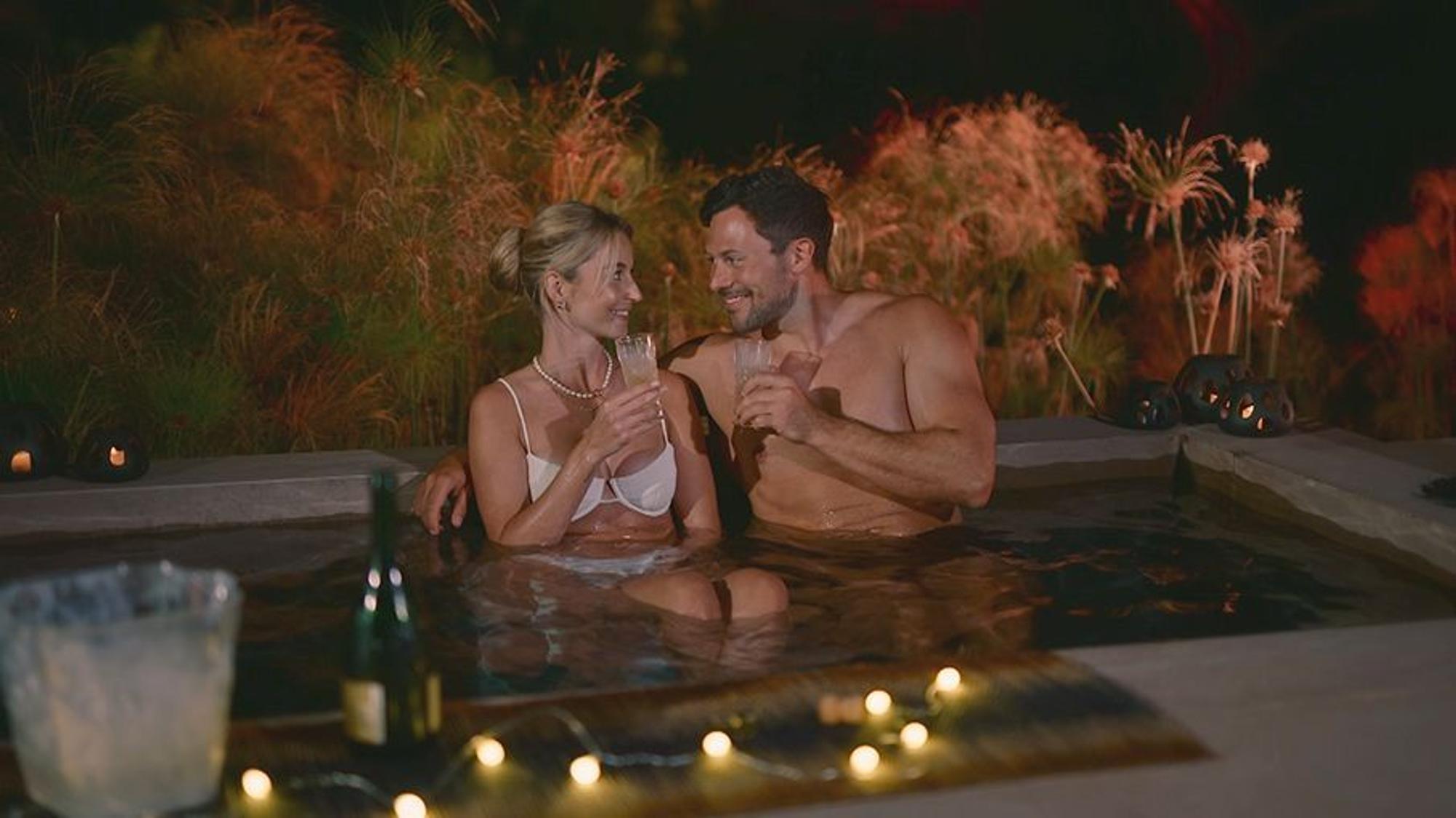 Eine Frau und ein Mann sitzen im Pool nebeneinander und lächeln sich an.