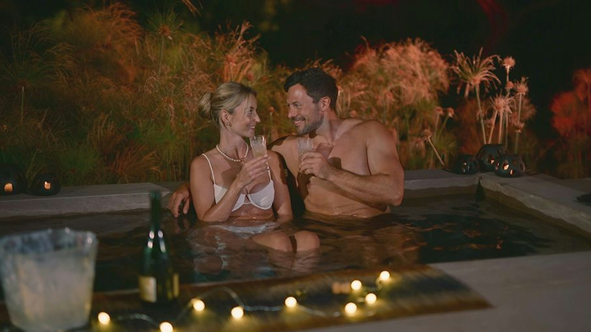 Eine Frau und ein Mann sitzen im Pool nebeneinander und lächeln sich an.