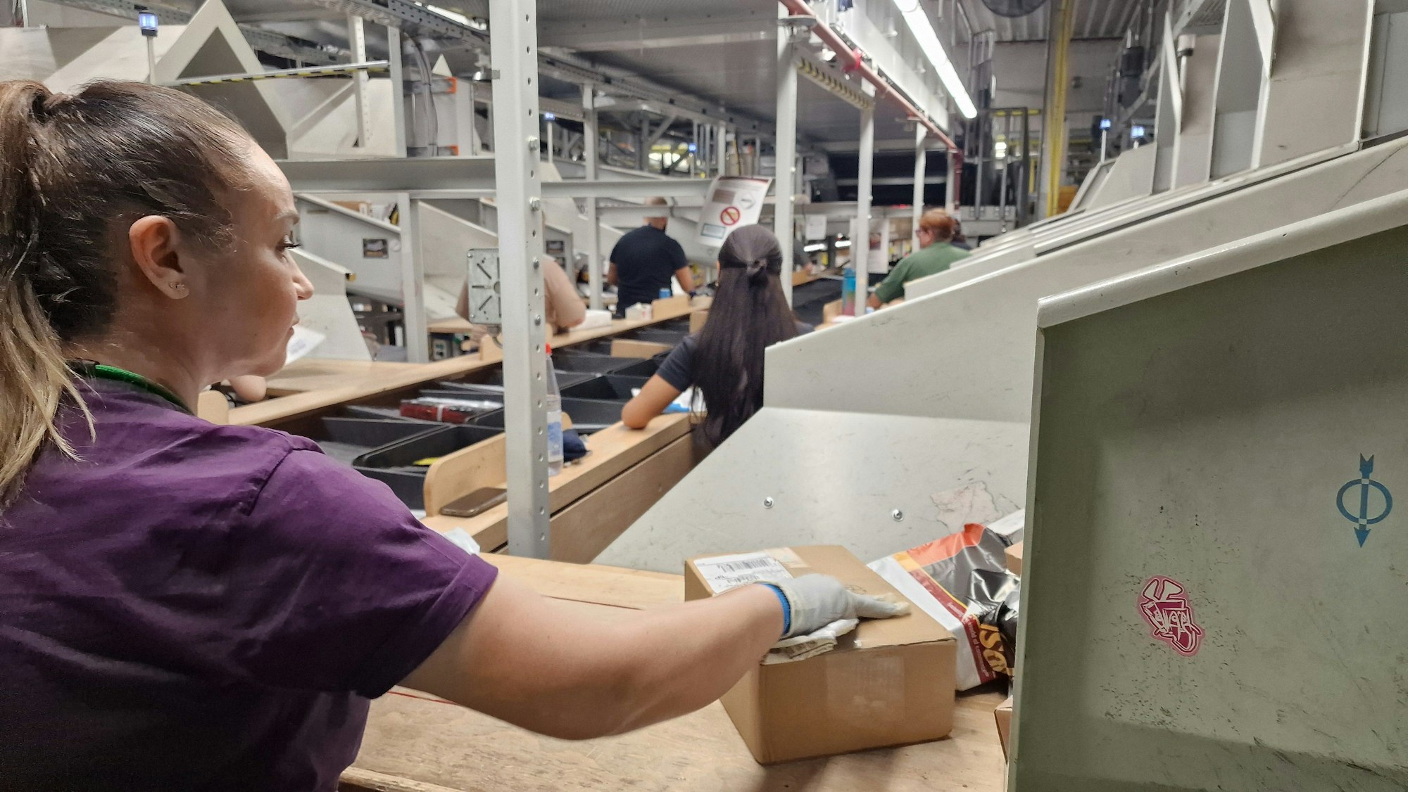 UPS Air Hub. Logistikzentrum mit Sortieranlage am Flughafen Köln/Bonn. Sortierung der kleinen Pakete auf Band mit Kippschalen durch Mitarbeitende.