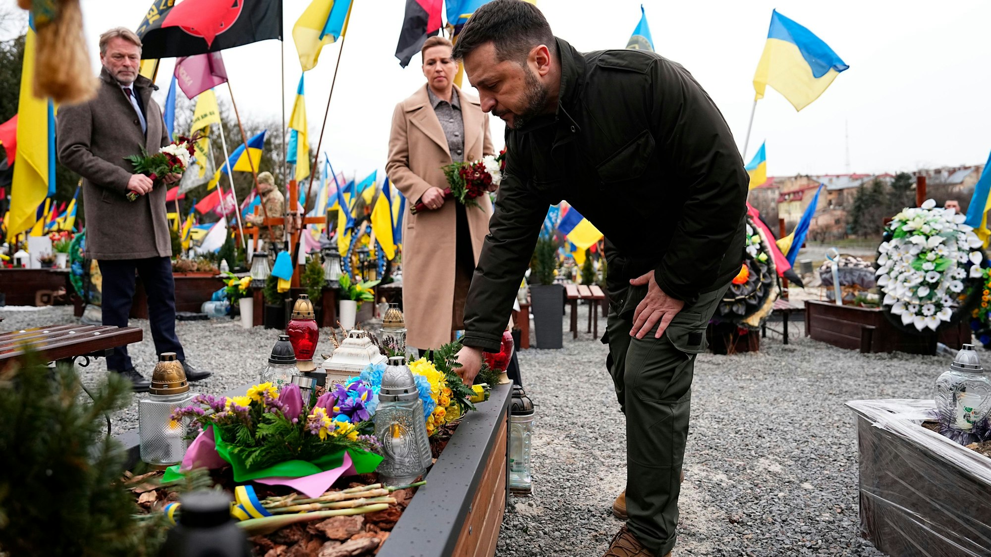 Wolodymyr Selenskyj (rechts), Präsident der Ukraine, legt neben Mette Frederiksen, Ministerpräsidentin von Dänemark, und ihrem Ehemann Bo Tengberg Blumen während einer Gedenkfeier auf dem Marsfeld auf dem Lytschakiwski-Friedhof in Lwiw nieder.