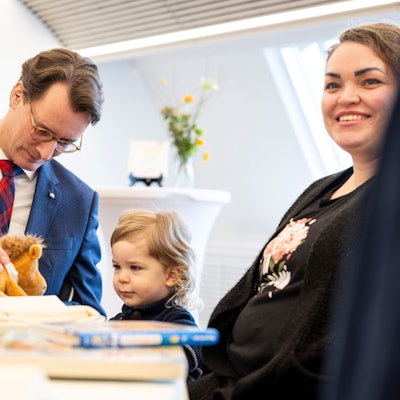 Hendrik Wüst (CDU), Ministerpräsident von Nordrhein-Westfalen, spielt am Tisch mit seinem Ehrenpatenkind Daniel, rechts Mutter Anna Marchenko.