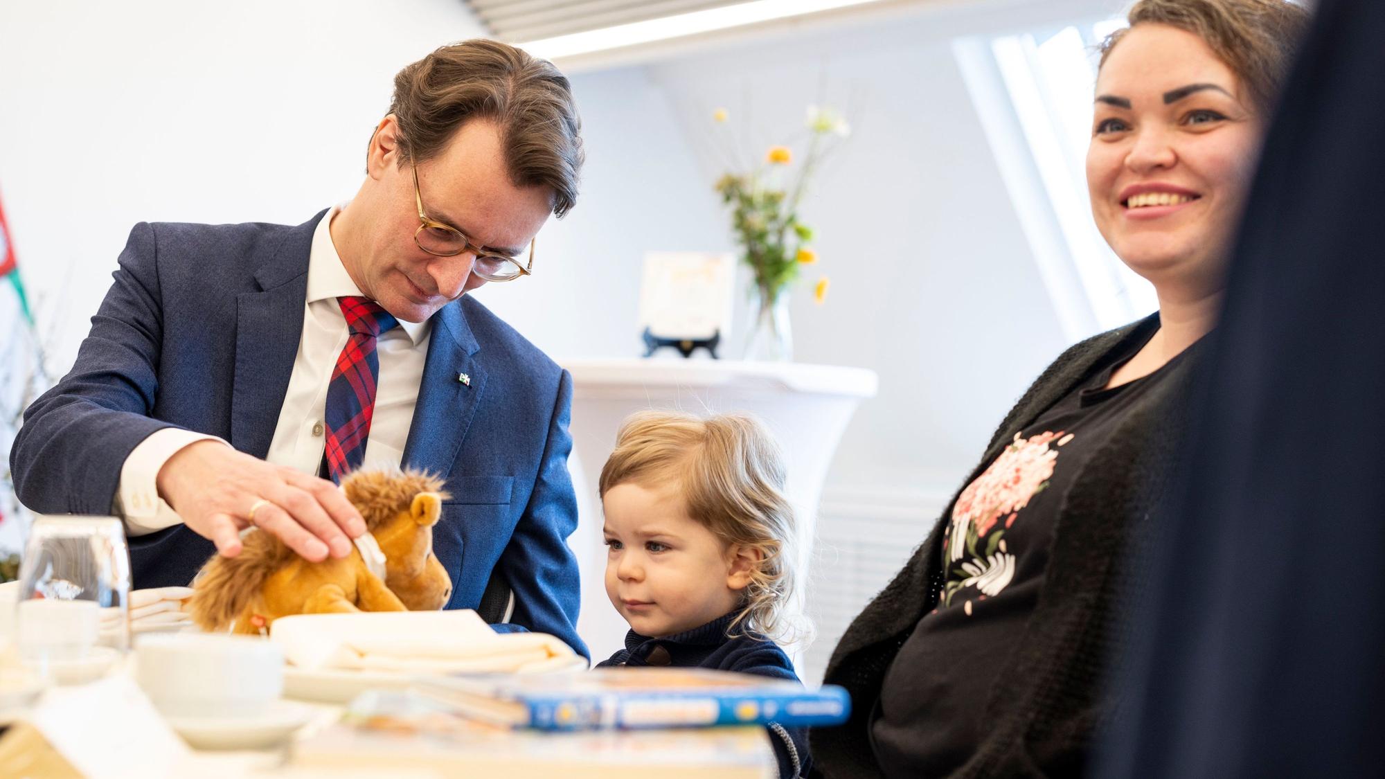Hendrik Wüst (CDU), Ministerpräsident von Nordrhein-Westfalen, spielt am Tisch mit seinem Ehrenpatenkind Daniel, rechts Mutter Anna Marchenko.