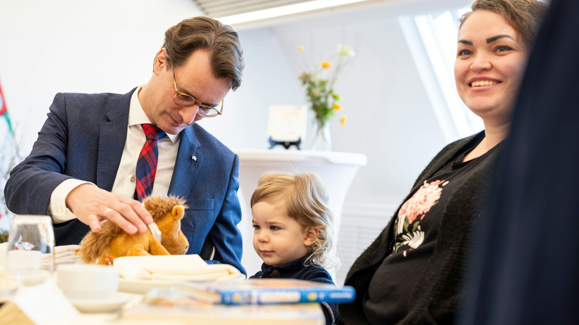 Hendrik Wüst (CDU), Ministerpräsident von Nordrhein-Westfalen, spielt am Tisch mit seinem Ehrenpatenkind Daniel, rechts Mutter Anna Marchenko.
