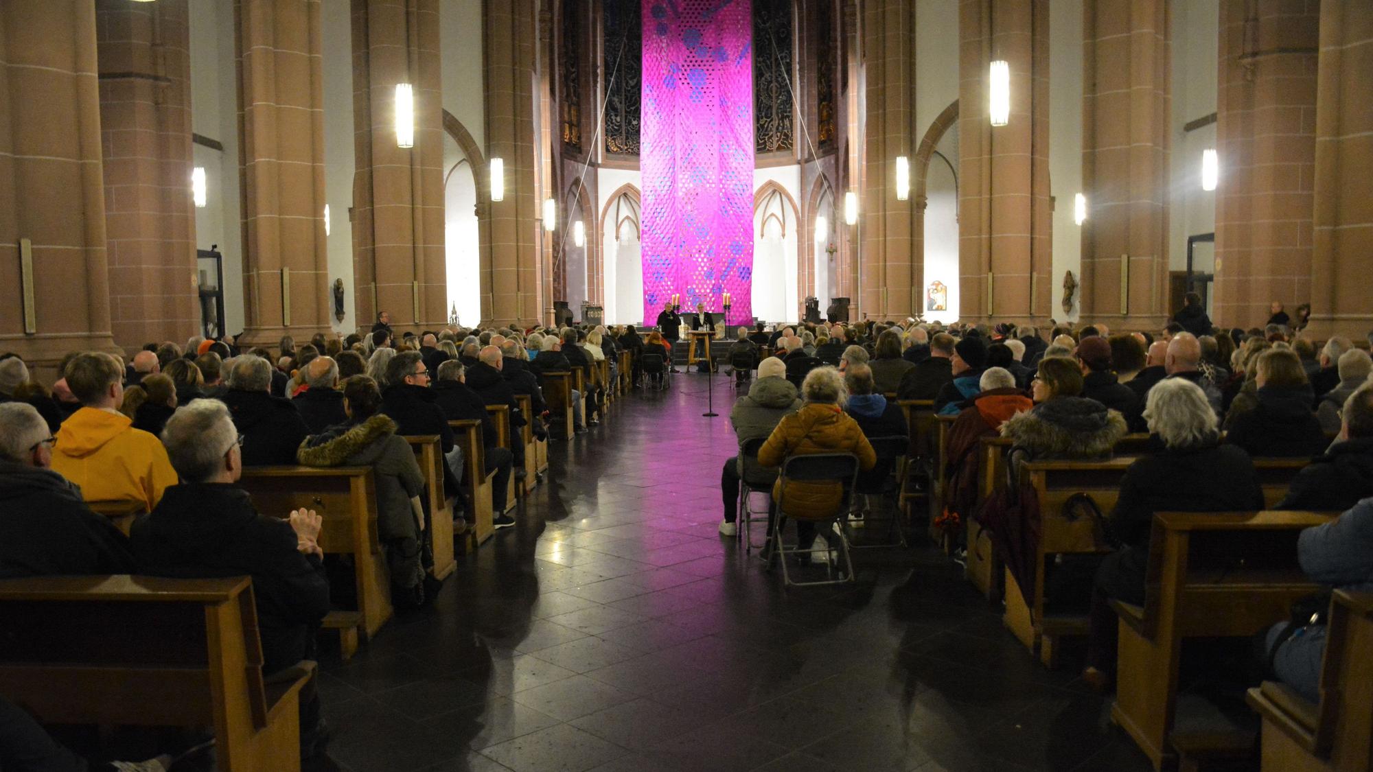 Ein voll besetzter Kirchenraum mit einer großen Kunst-Installation im Hintergrund.