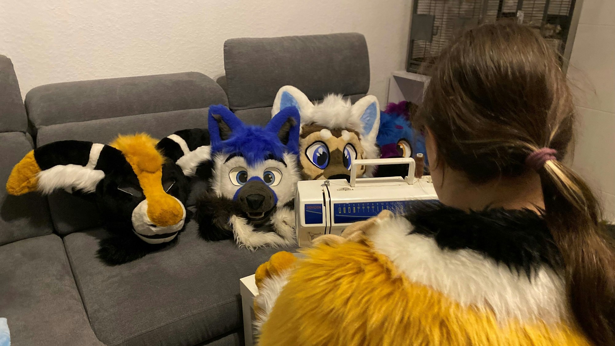 Selina Klein sitzt im Wohnzimmer an einer Nähmaschine. Auf einer Couch liegen selbst genähte Tierköpfe.