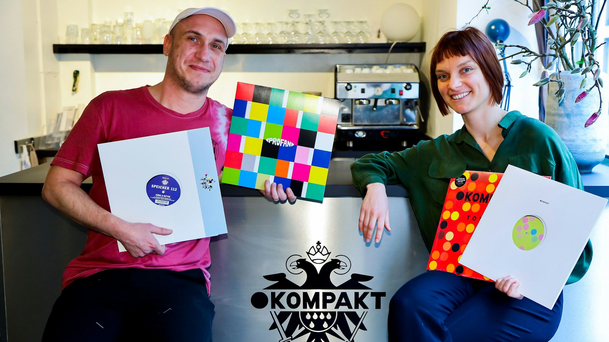 Ein Mann und eine Frau sitzen an einer Theke, sie haben Schallplatten in den Händen.