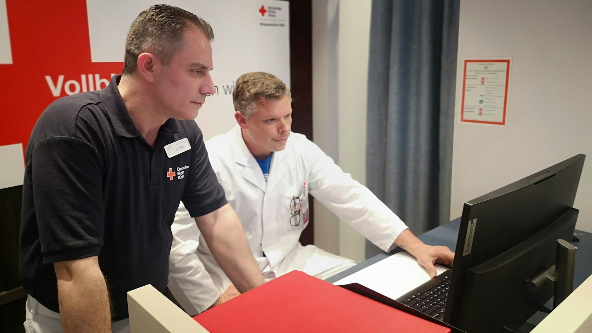 Zwei Mitarbeiter der Blutspende beugen sich an einem Tisch über einen Computerbildschirm.