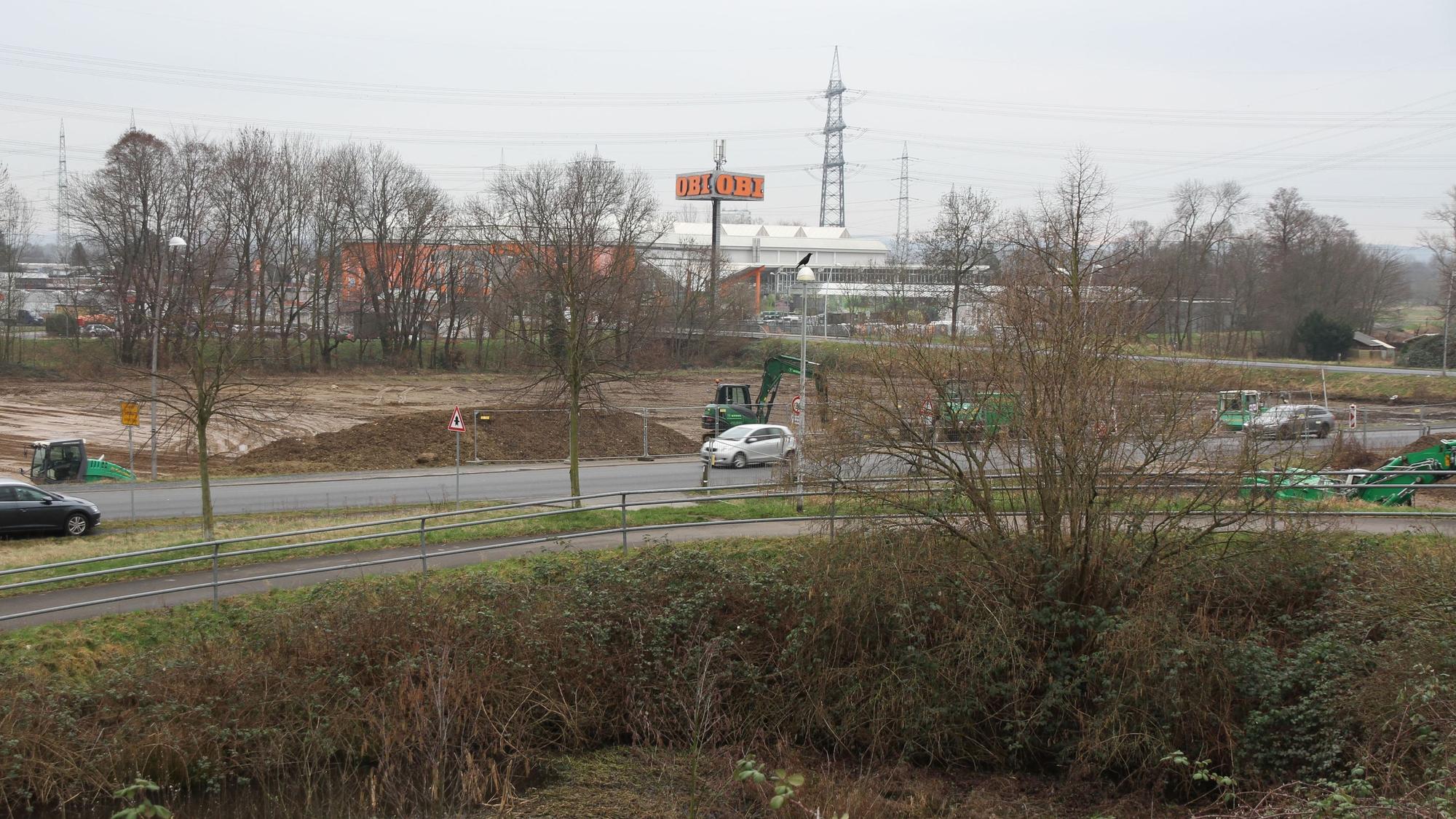 Eine Straße vor einem großen Baufeld mit grünen Baggern.
