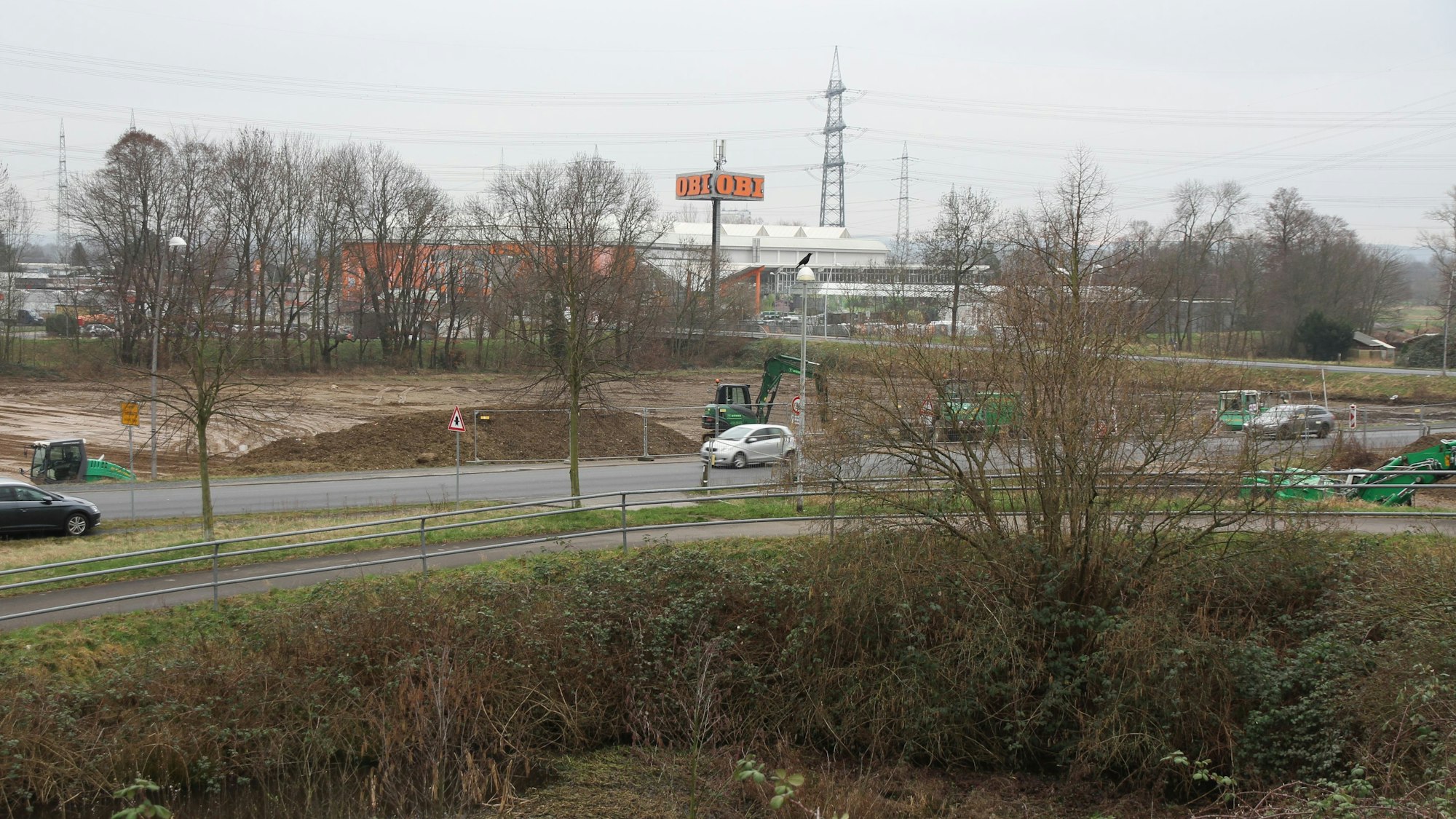 Eine Straße vor einem großen Baufeld mit grünen Baggern.