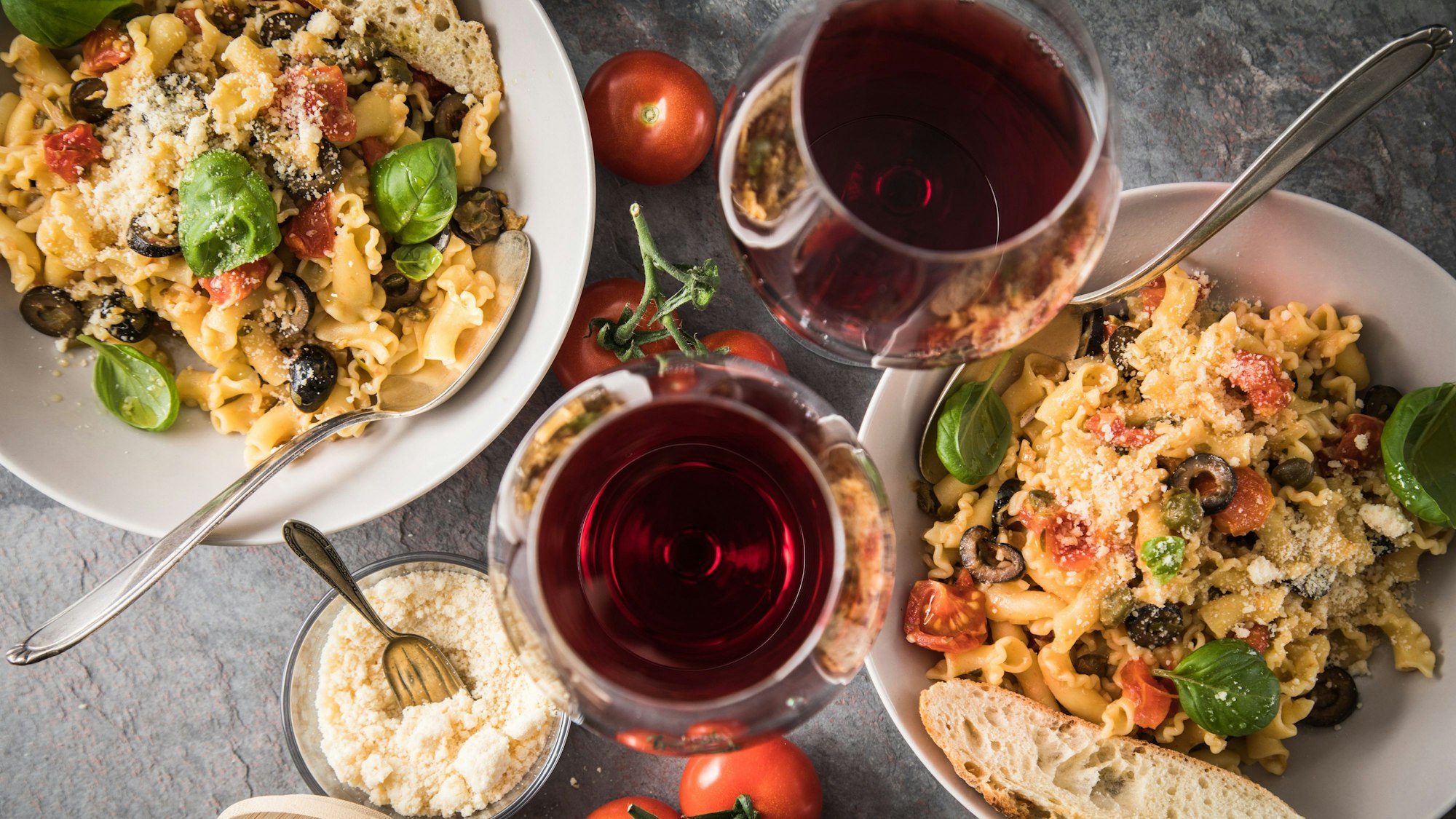 Zwei Gläser Rotwein und zwei Portionen Pasta stehen auf einem Tisch. (Symbolbild)