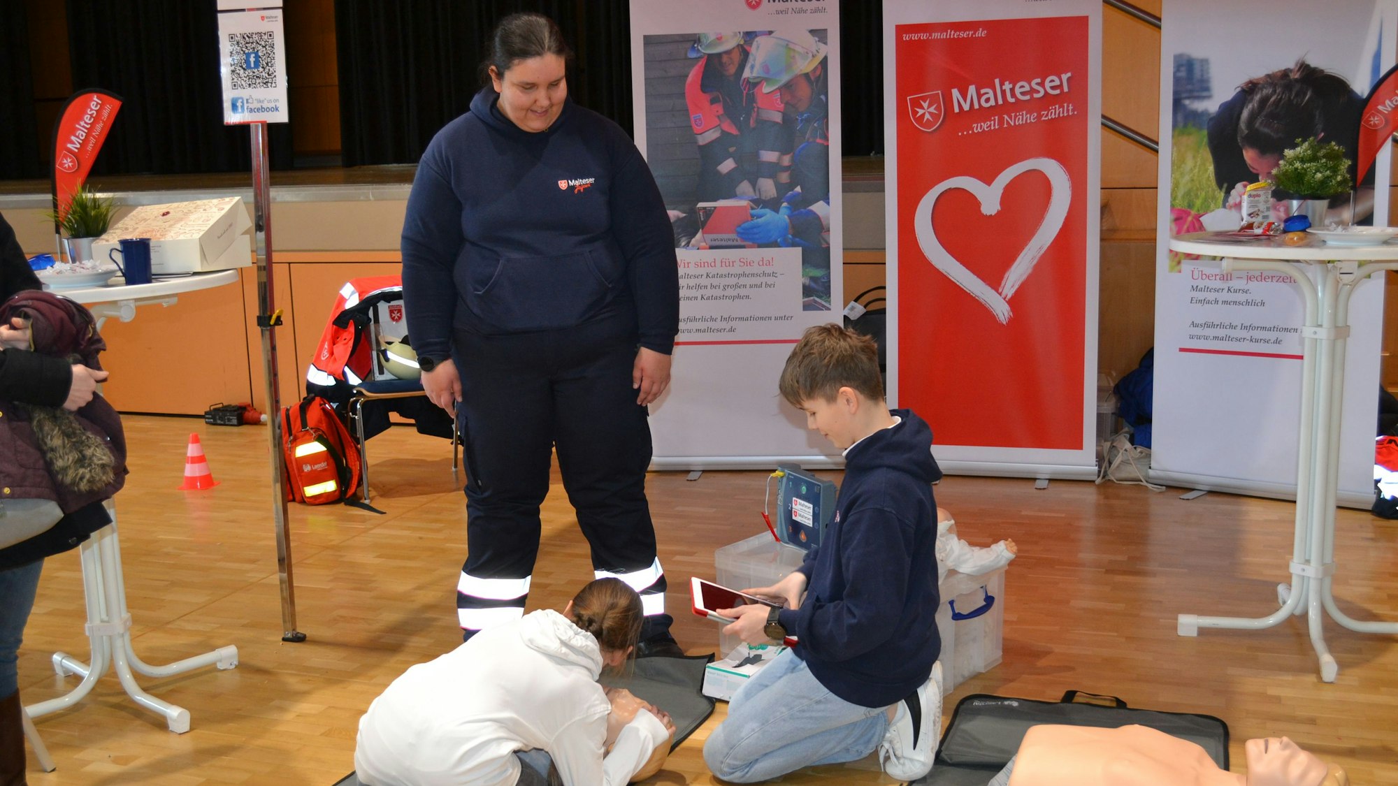 Ein Junge und ein Mädchen knien am Boden. Sie üben an einer Puppe die Herzmassage.