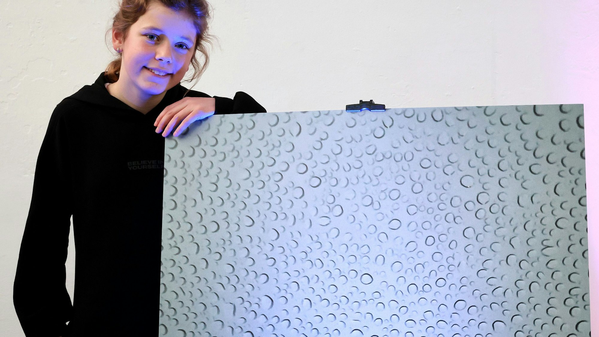 Emilie Bings posiert mit ihrem Bild. Es zeigt eine Glasscheibe voller Regentropfen.