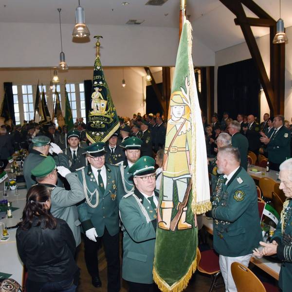 Männer in grünen Uniformen tragen Fahnen in einen Saal.
