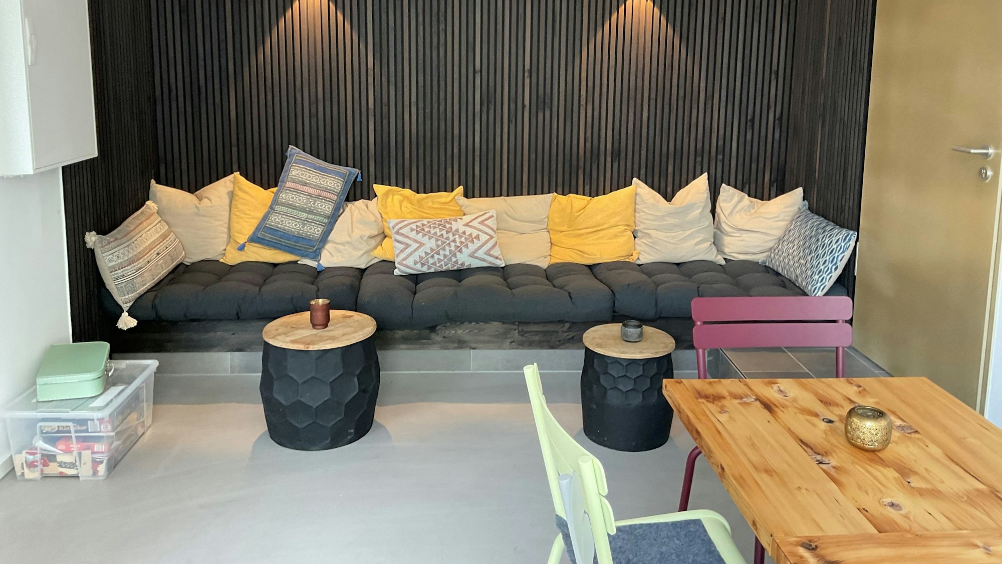 Signcafé in Köln: Eine Sitzecke mit vielen Kissen, davor zwei Sofatische, davor ein Tisch mit Stühlen.