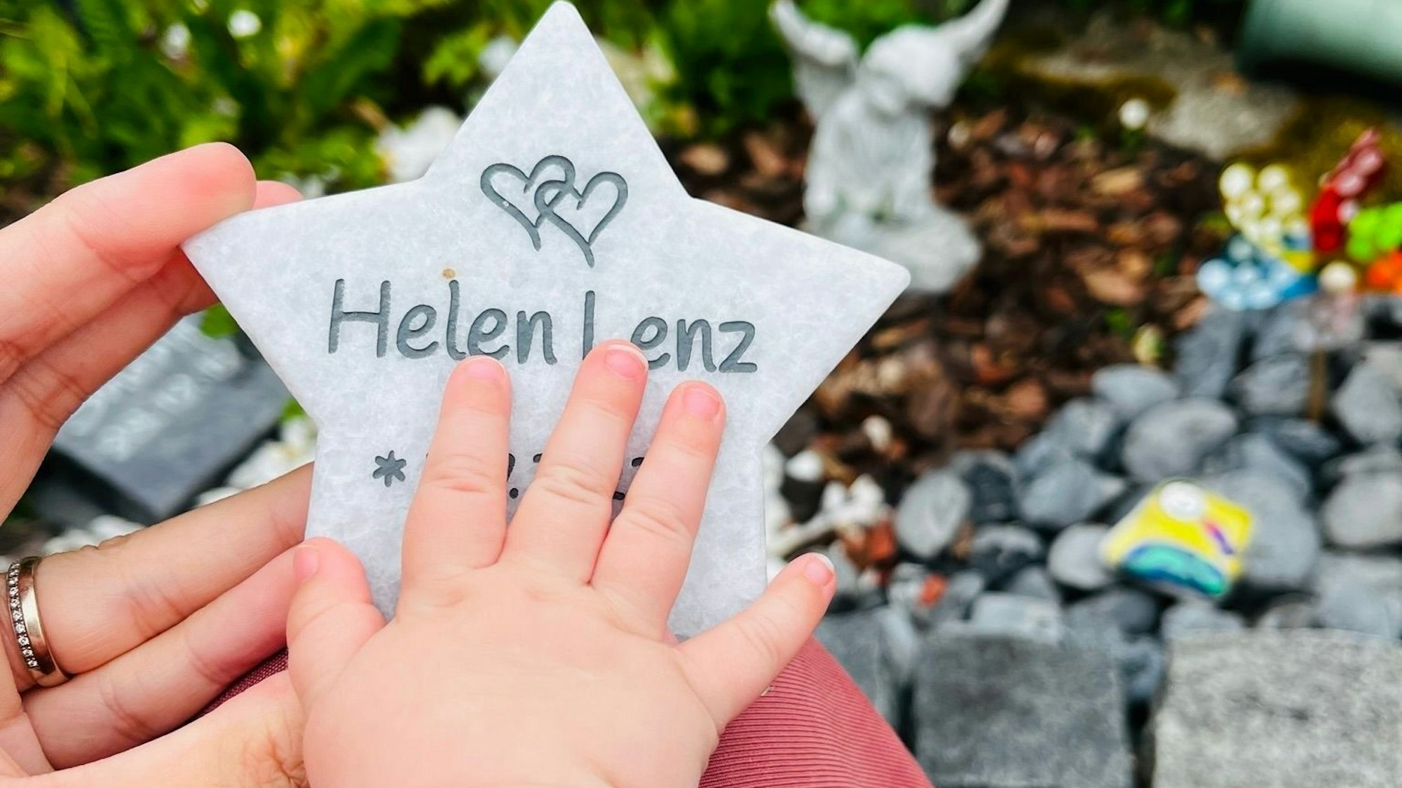 Das Bild zeigt die Babyhand von Jana. Sie liegt auf einem Steinstern, auf dem der Name des toten Zwillings eingraviert ist.