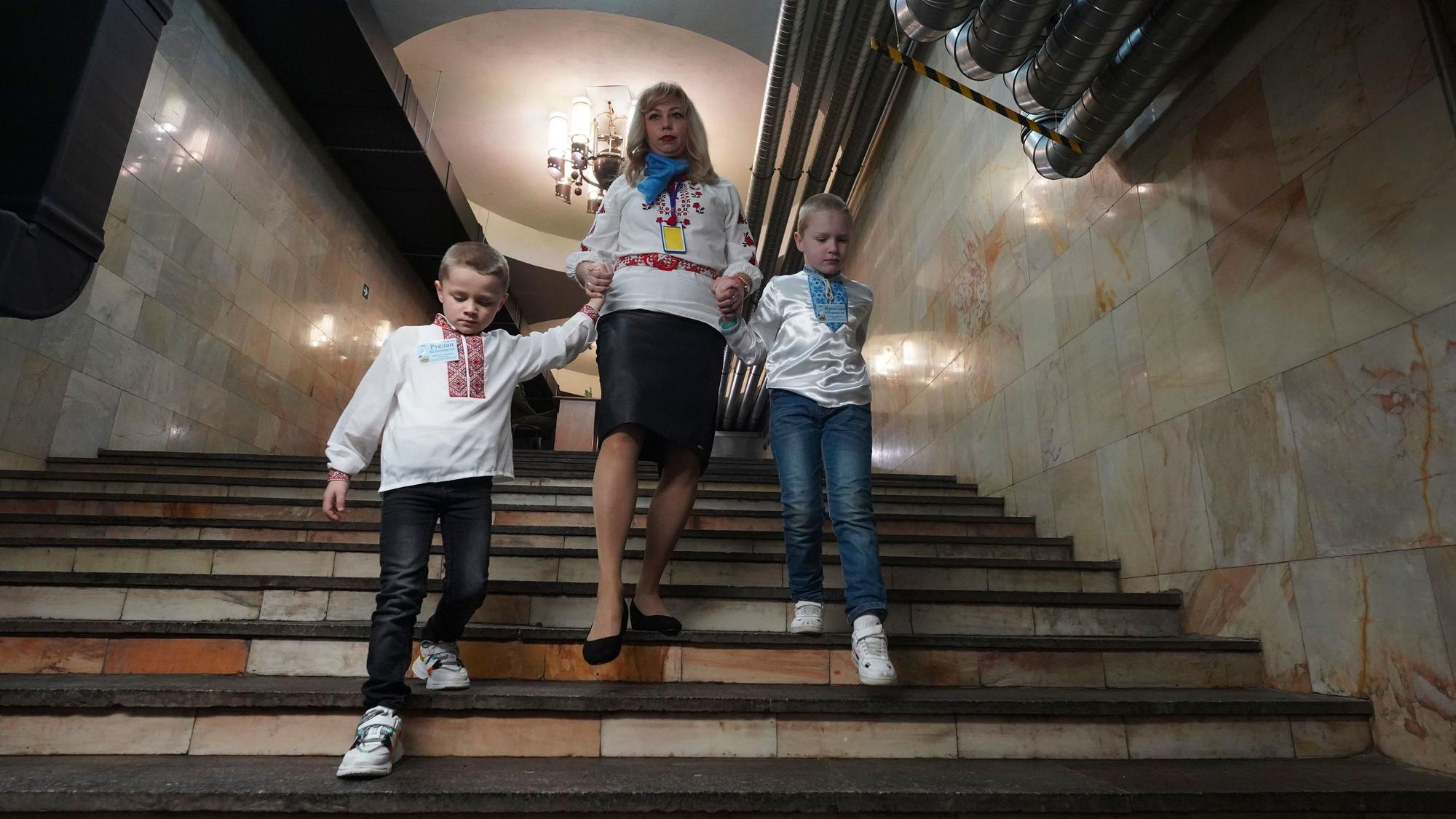 Eine Erzieherin hält die Hände von Kindern, während sie im Januar 2024 in Charkiw die Treppe zu einem unterirdischen Kindergarten in einer U-Bahn-Station hinuntergehen.