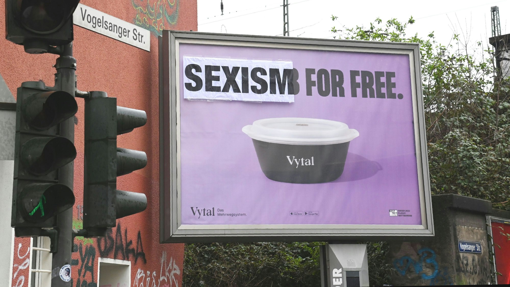 Auf einem violetten Plakat steht über einer Mehrwegschüssel „Sexism for free“. Das Wort „Sexism“ wurde nachträglich über das Plakat geklebt.