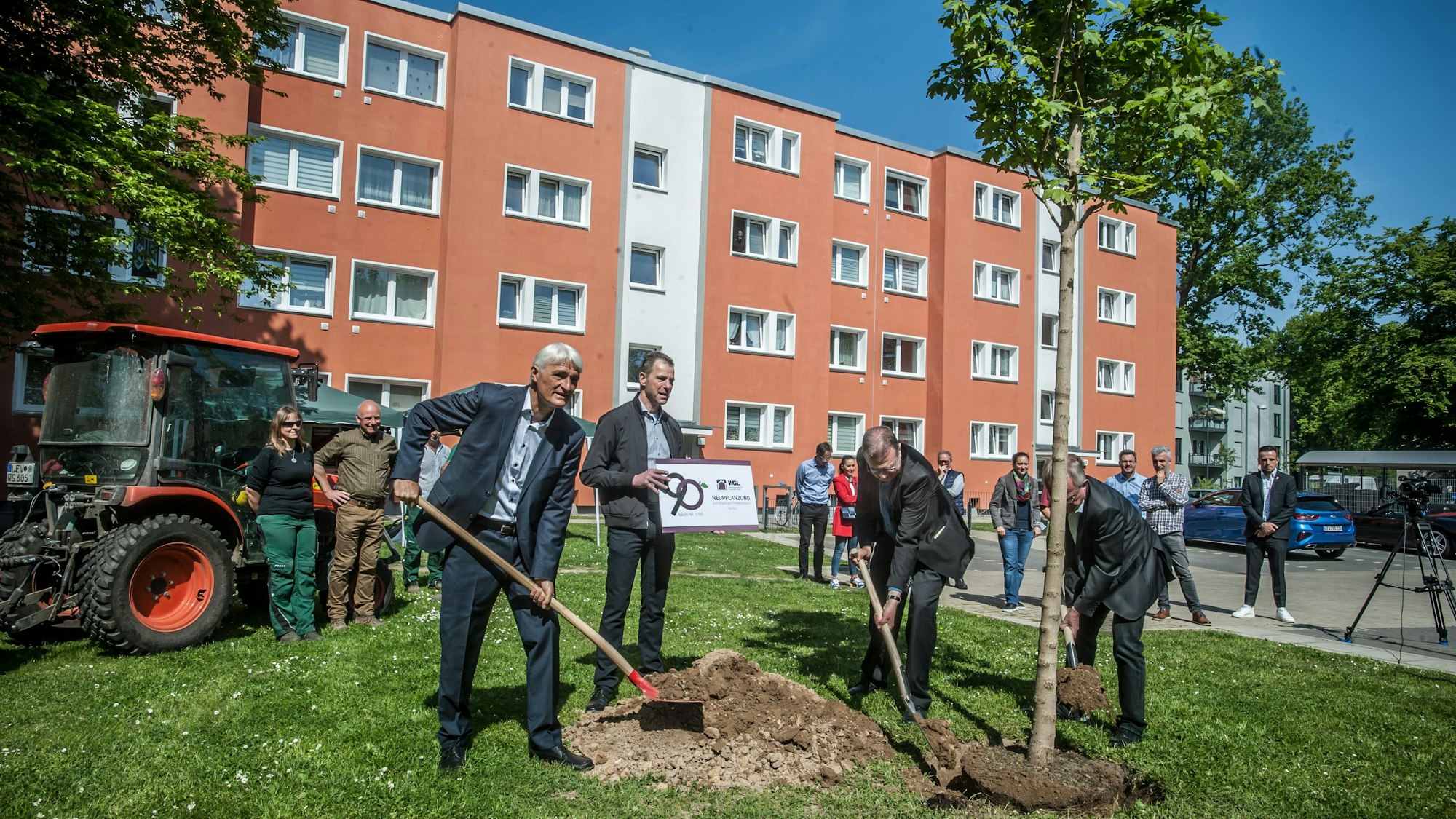 Vier Männer pflanzen einen Baum vor einem Mehrfamilienhaus.