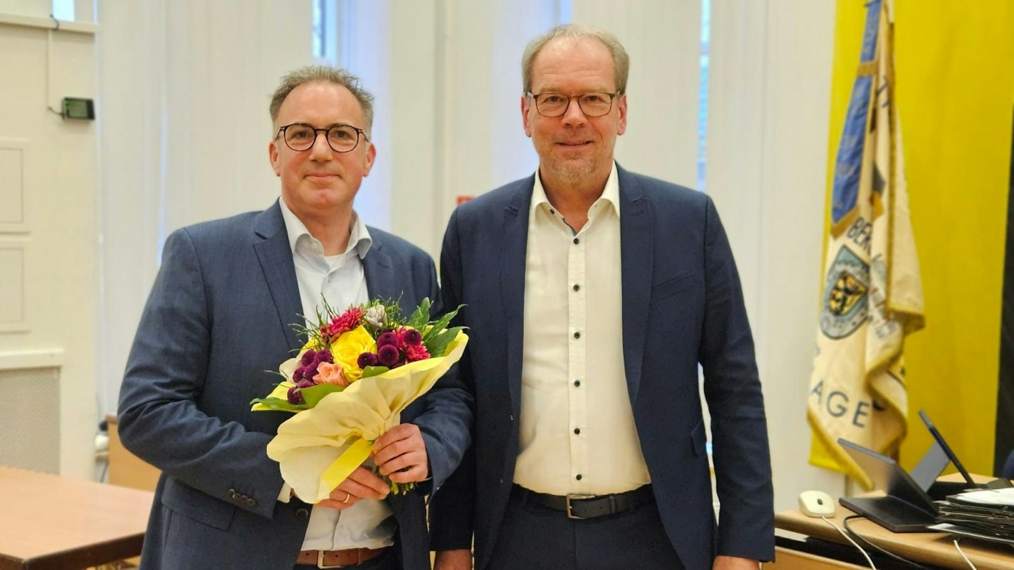 Zwei Männer stellen sich für das Foto auf, einer hält einen Blumenstrauß.