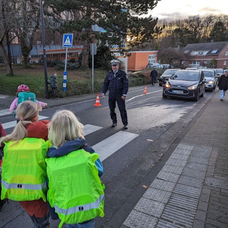 Schulkinder gehen im Beisein eines Polizisten über einen Zebrastreifen.