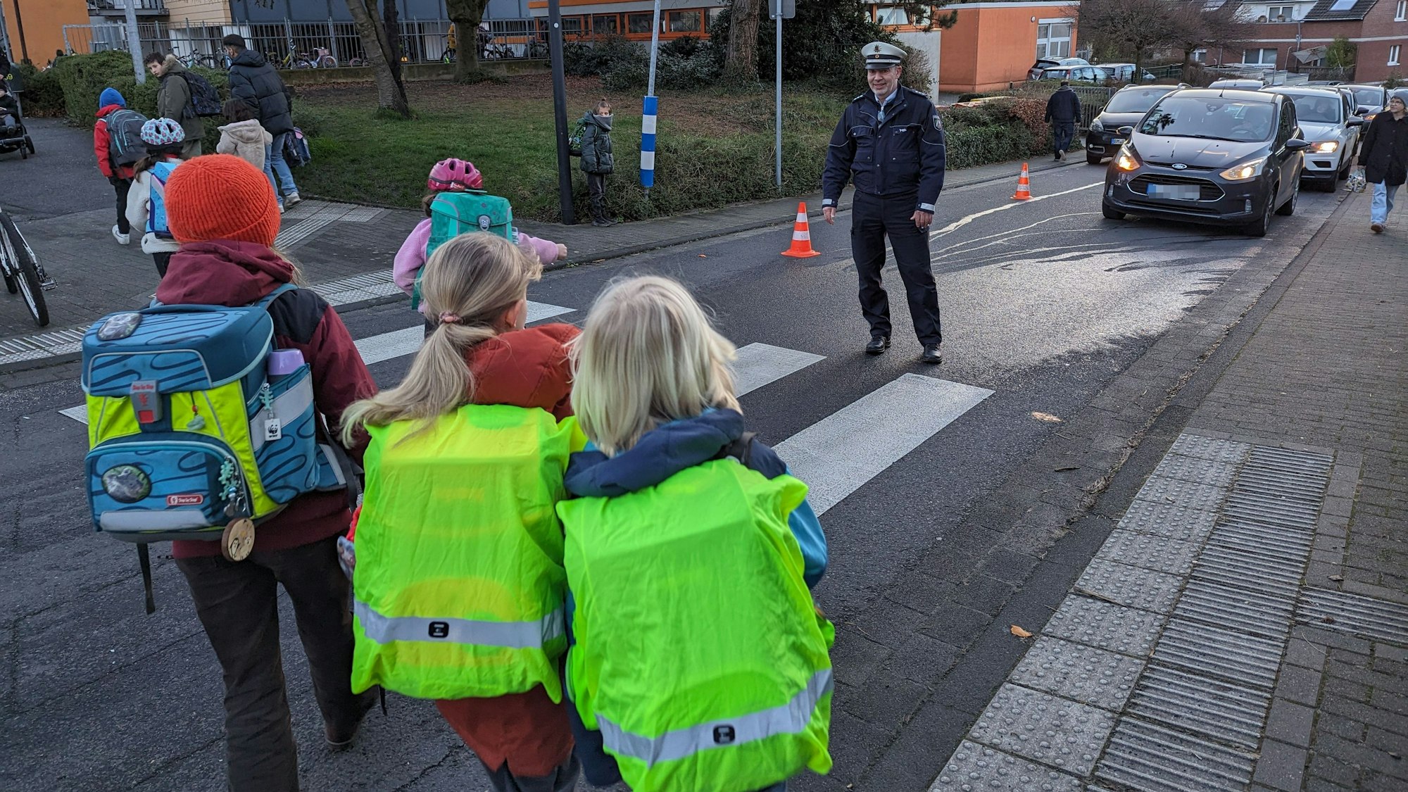 Schulkinder gehen im Beisein eines Polizisten über einen Zebrastreifen.