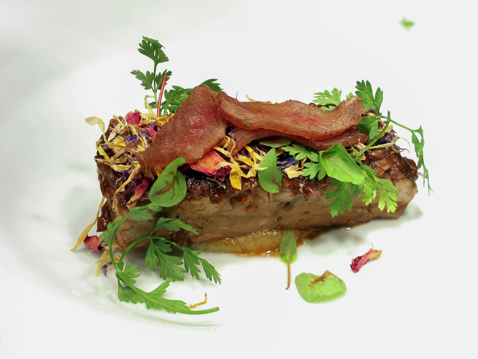 Eine mit Blüten dekorierte Portion von Lammfleisch auf einem Teller.