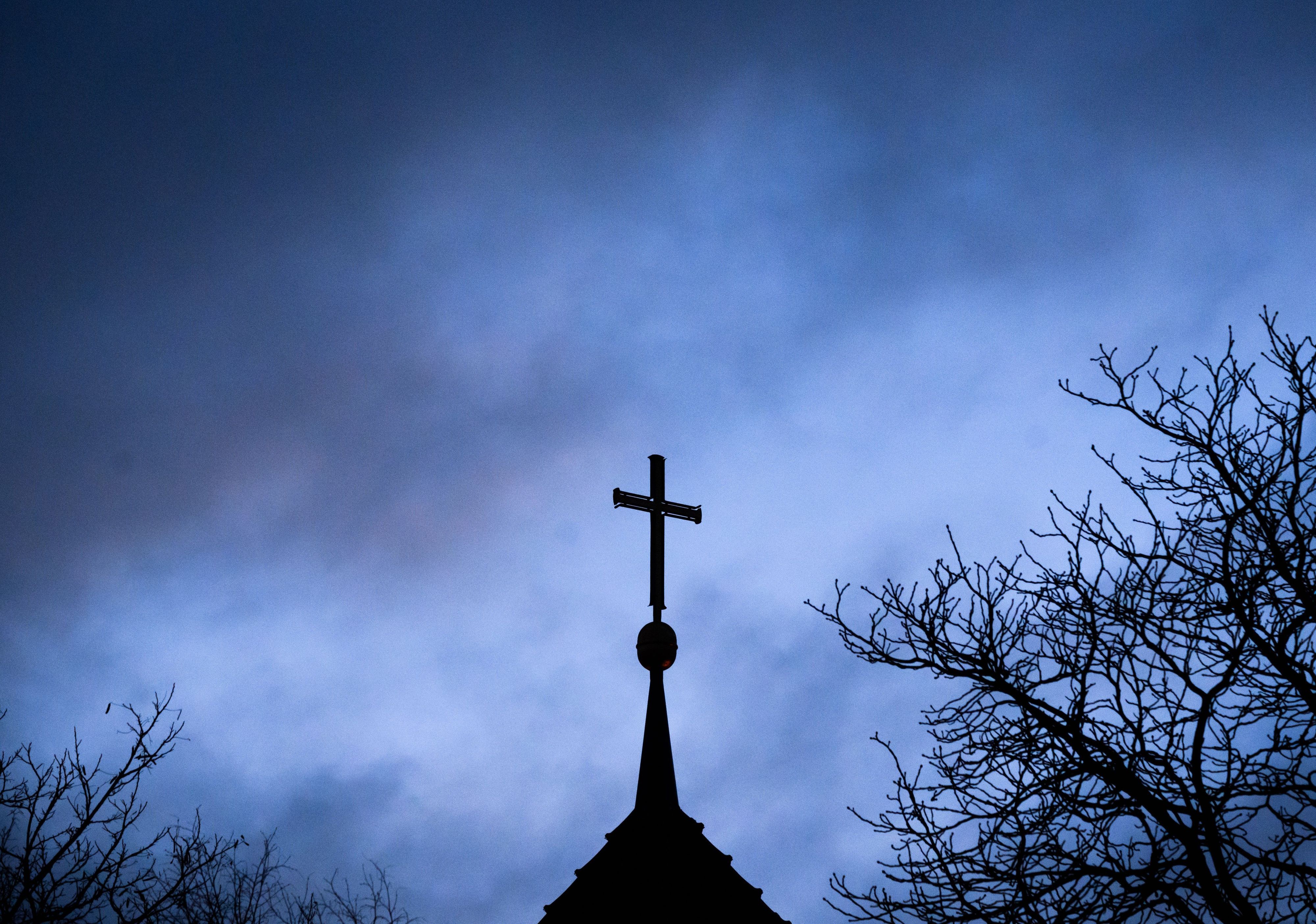 Dunkle Wolken ziehen über das Kreuz auf einer evangelischen Kirche.