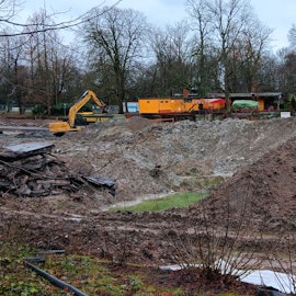 Ein Bagger steht auf dem Grund des Volksgartenweihers inmitten größerer Schlammberge.